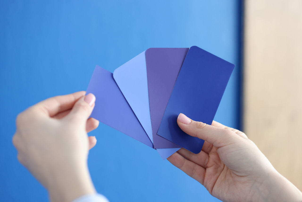 In hands of palette with blue shades against blue wall. Selection of paint for walls and facades concept