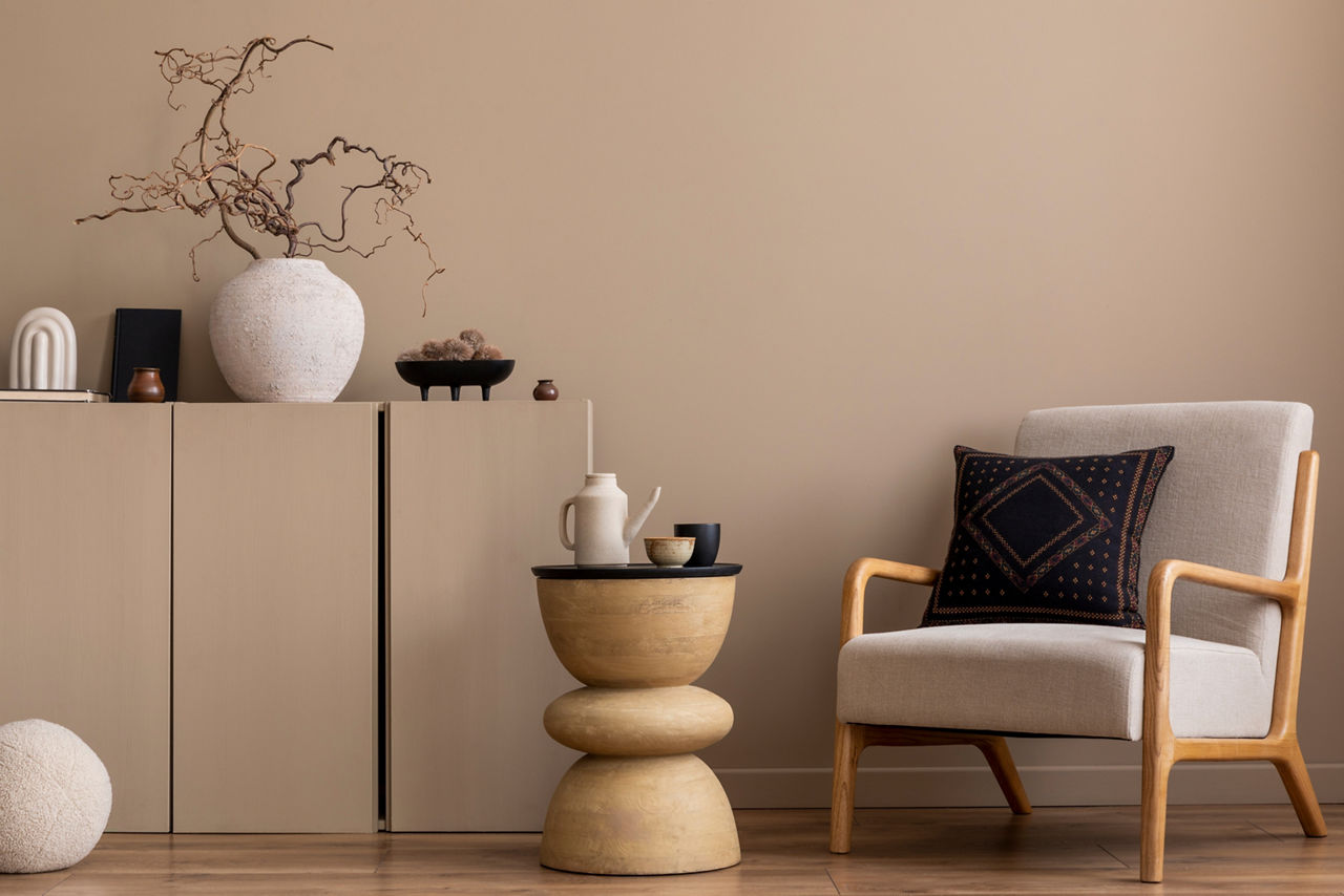 Cozy composition of living room interior with gray armchair, dark pillow, beige sideboard, wooden coffee table, vase with branch, round pillow and personal accessories. Home decor. Template.